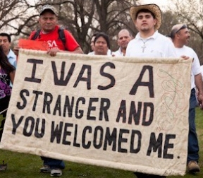 2 men holding sign: "I was a stranger and you welcomed me."